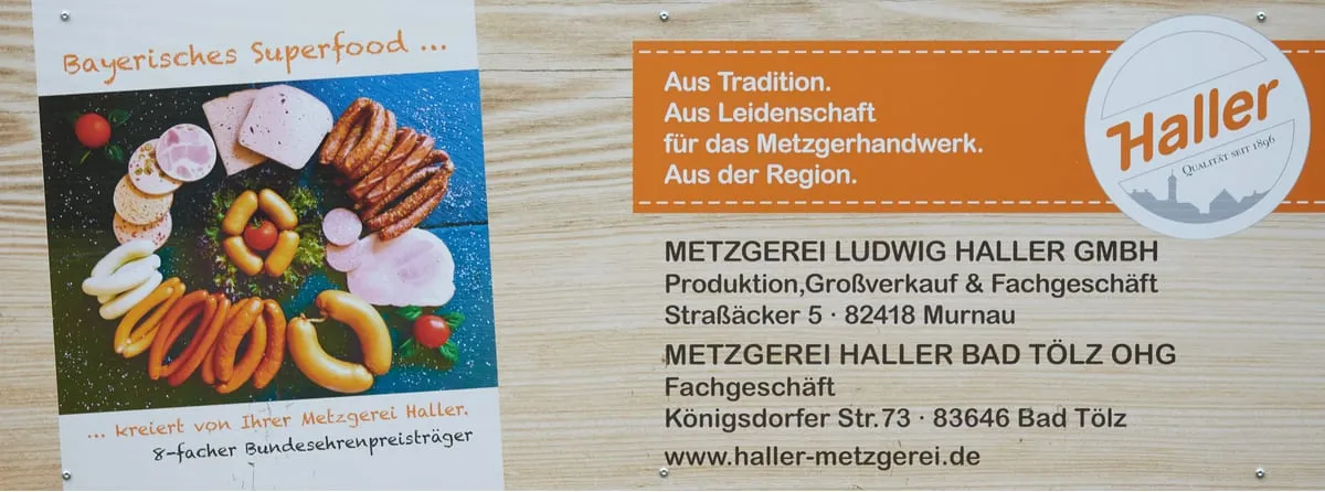Bandenwerbung der Metzgerei Haller mit einer Platte bayerischer Wurstspezialitäten